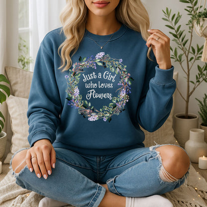 Blonde woman in a blue crewneck sweatshirt with "Just a Girl who loves Flowers" in a floral wreath design.
