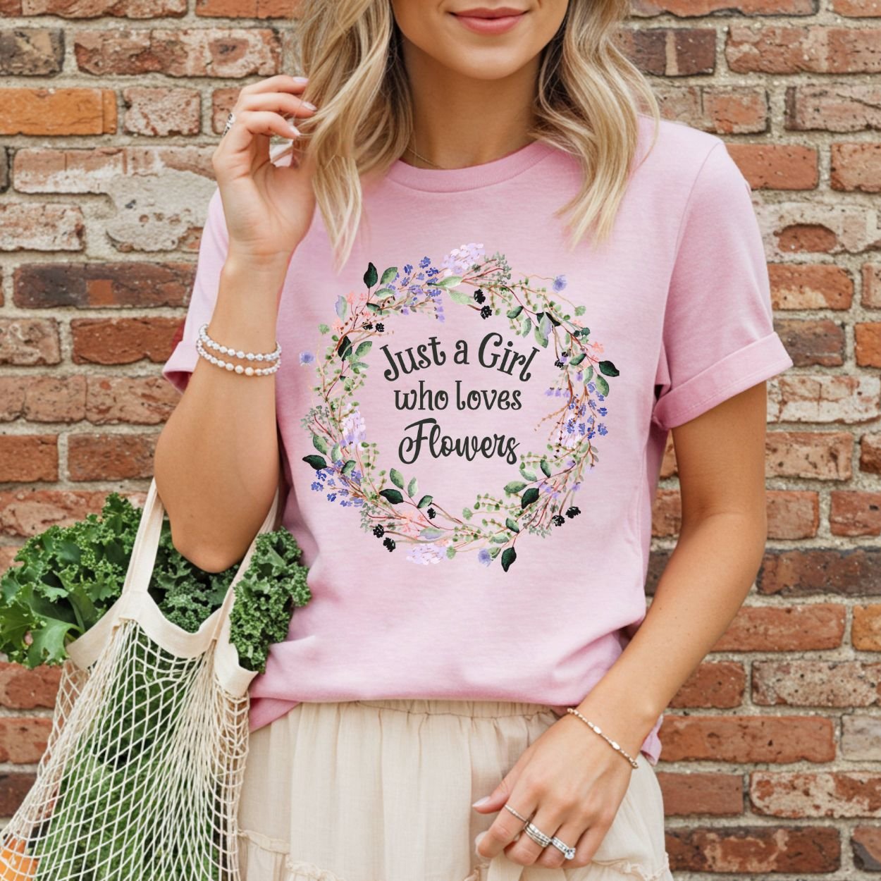 Pink "Just a Girl who Loves Flowers" t-shirt with a watercolor floral wreath design, worn by a woman holding kale.