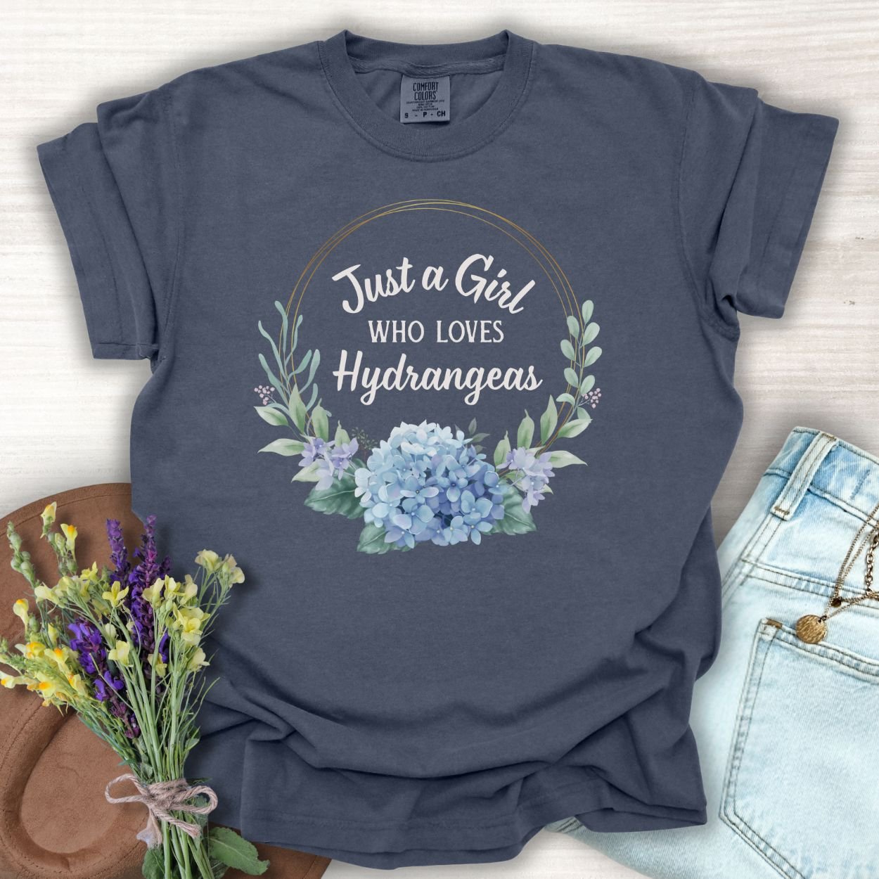 Denim blue garment-dyed cotton t-shirt with "Just a Girl Who Loves Hydrangeas" text and watercolor hydrangeas.