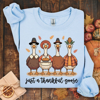 Light blue S sweatshirt with pilgrim ducks, apple pie, and "just a thankful goose" text, surrounded by autumn decor.