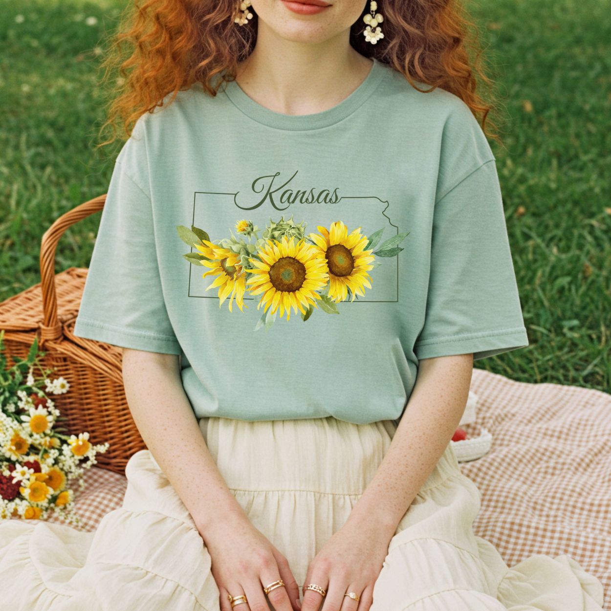 Garment-dyed sage green t-shirt with Kansas outline, "Kansas" script, and golden sunflowers.