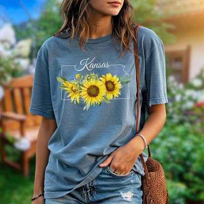 Garment-dyed blue cotton t-shirt with Kansas state outline, "Kansas" text, and golden sunflower graphic.