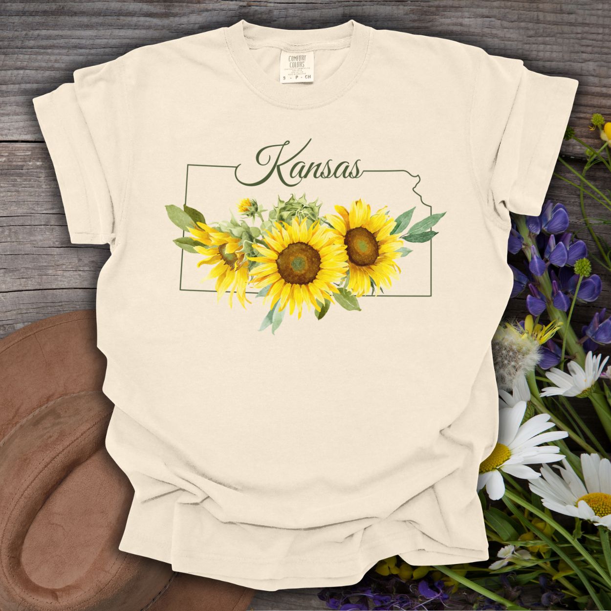 Ivory S t-shirt with a Kansas state outline and watercolor sunflowers, on a rustic wood background.