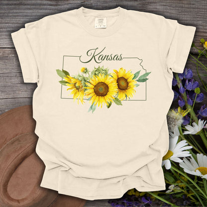 Ivory S t-shirt with a Kansas state outline and watercolor sunflowers, on a rustic wood background.