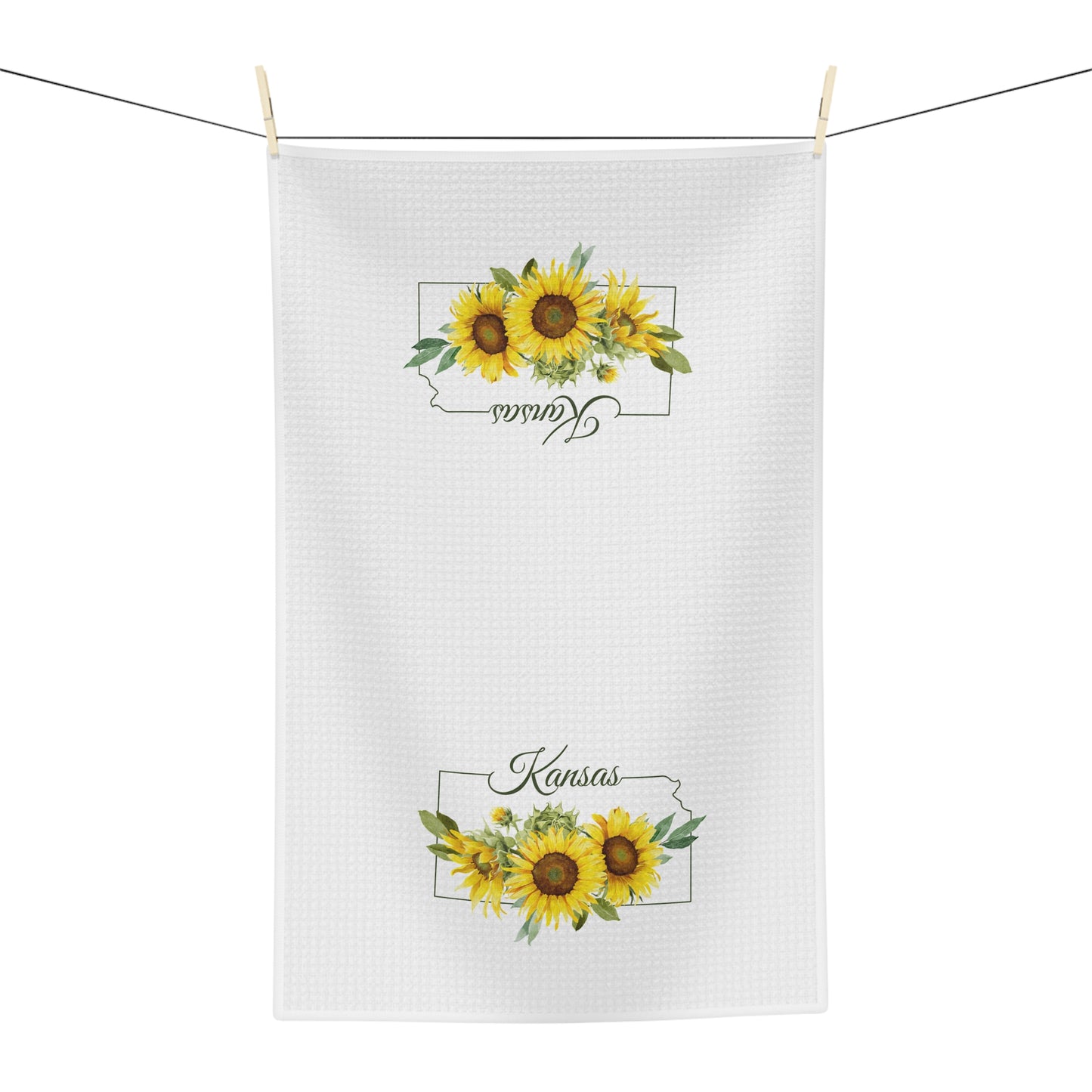 White microfiber tea towel with "Kansas" and golden sunflowers, hanging on a line.