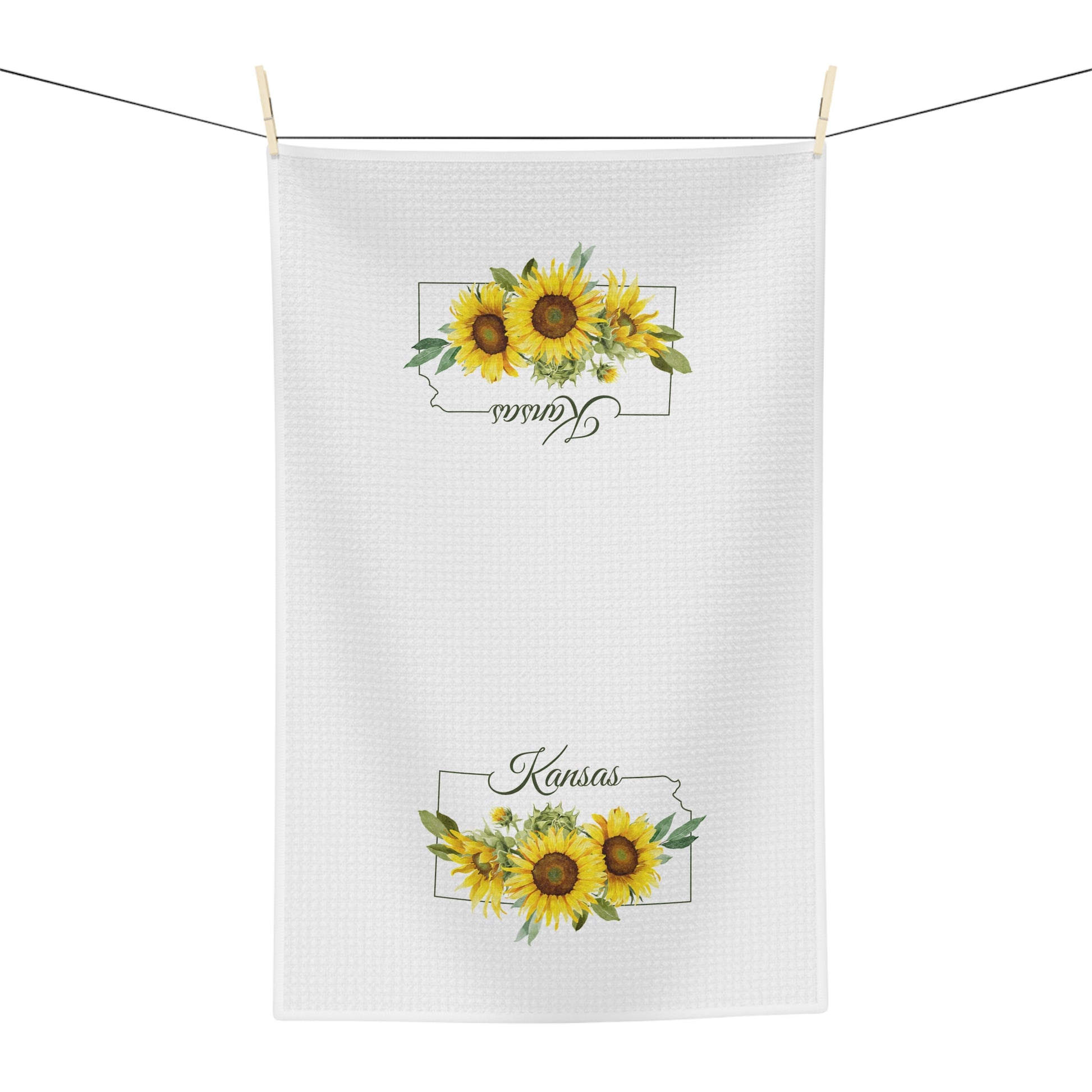 White microfiber tea towel with "Kansas" and golden sunflowers, hanging on a line.