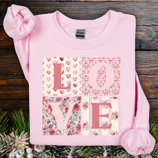 Light pink crewneck sweatshirt with "LOVE" in cottagecore patchwork-style fabrics, on a wooden background with pine.