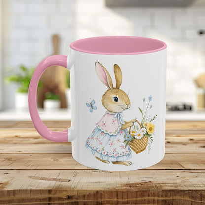 White ceramic mug with pink handle and interior, featuring a watercolor bunny in a floral dress holding a flower basket.