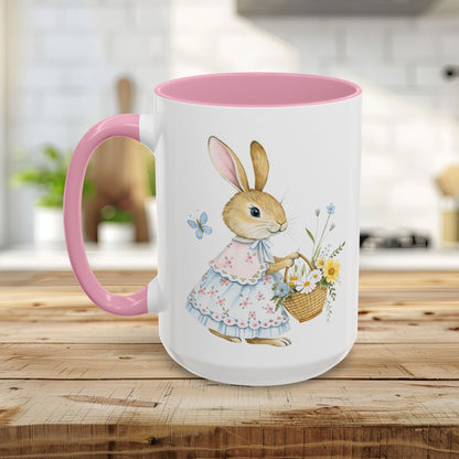 White ceramic mug with pink handle and interior, featuring a watercolor bunny in a dress holding a flower basket.