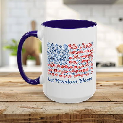White ceramic mug with blue handle/interior, featuring a floral flag design and "Let Freedom Bloom" text.