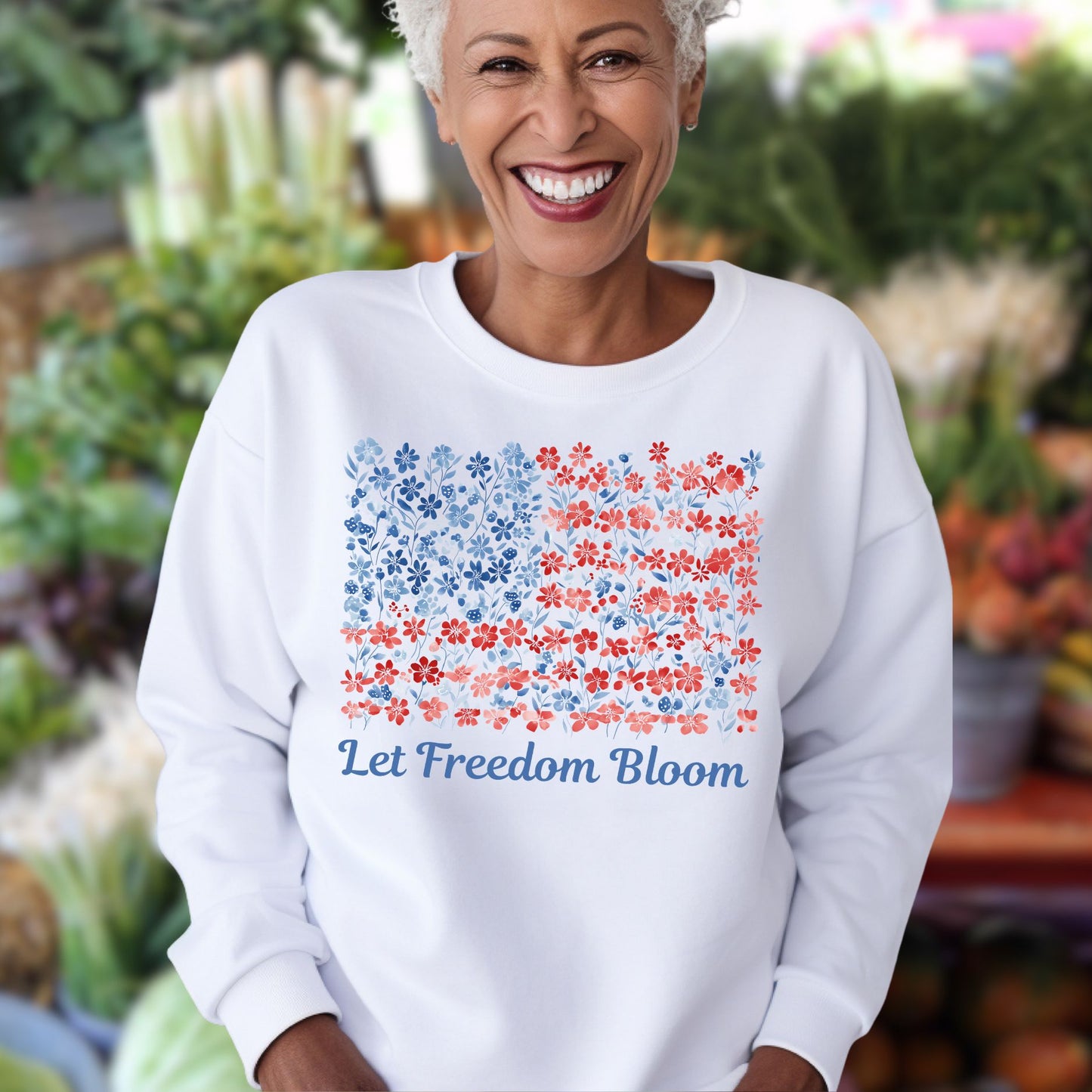 Smiling woman in white crewneck sweatshirt with a floral flag design and "Let Freedom Bloom" text.