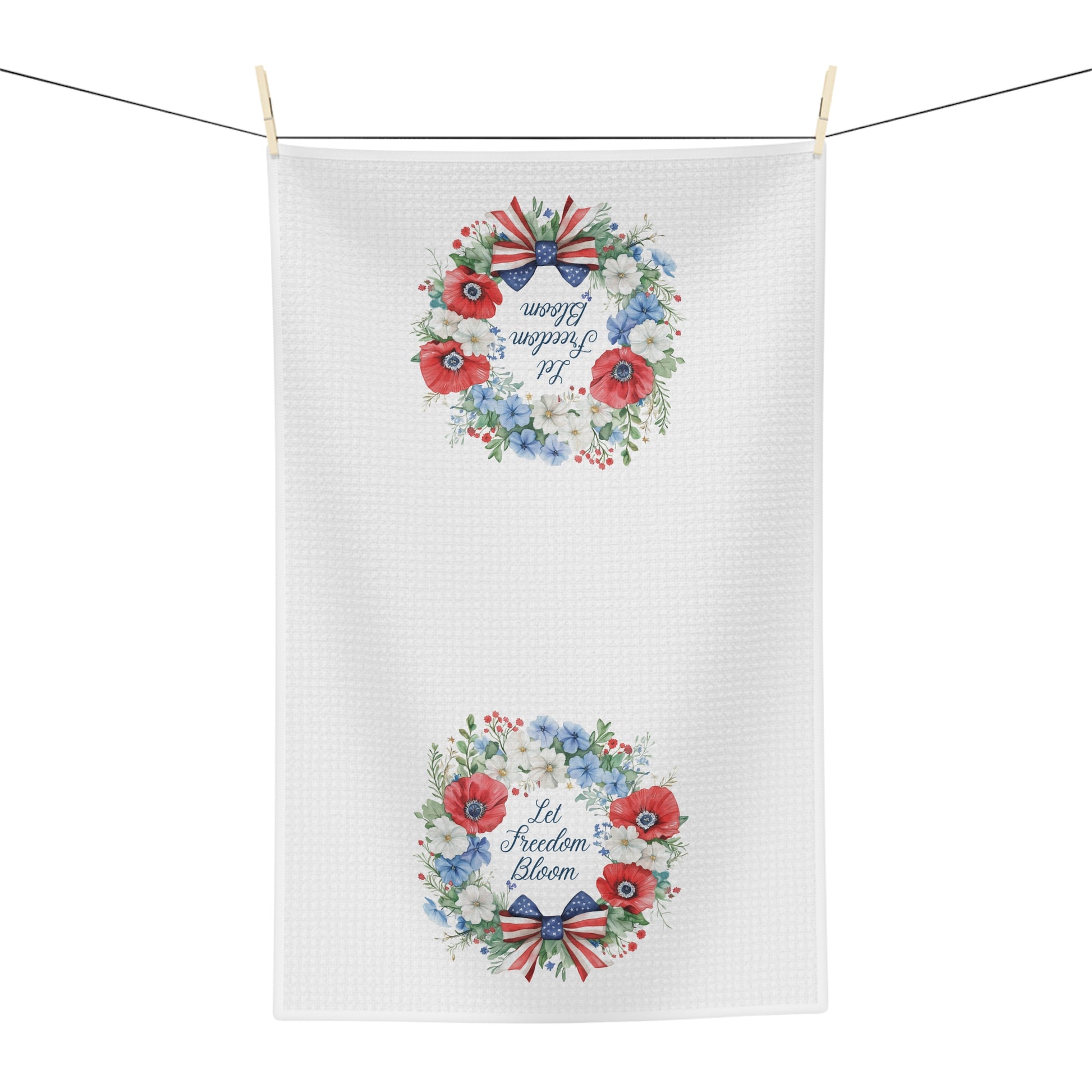 White microfiber tea towel with two watercolor wreaths of red, white, and blue florals and "Let Freedom Bloom.
