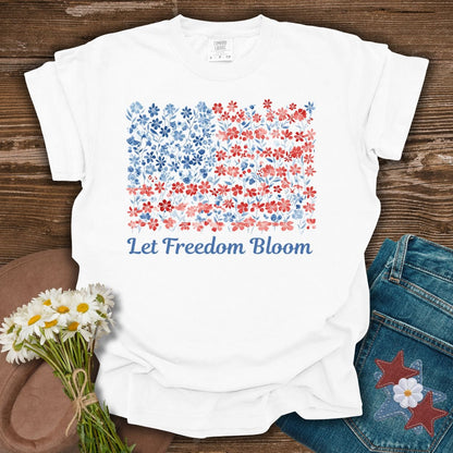 White S-size t-shirt with a floral USA flag design and "Let Freedom Bloom" text, on wood.