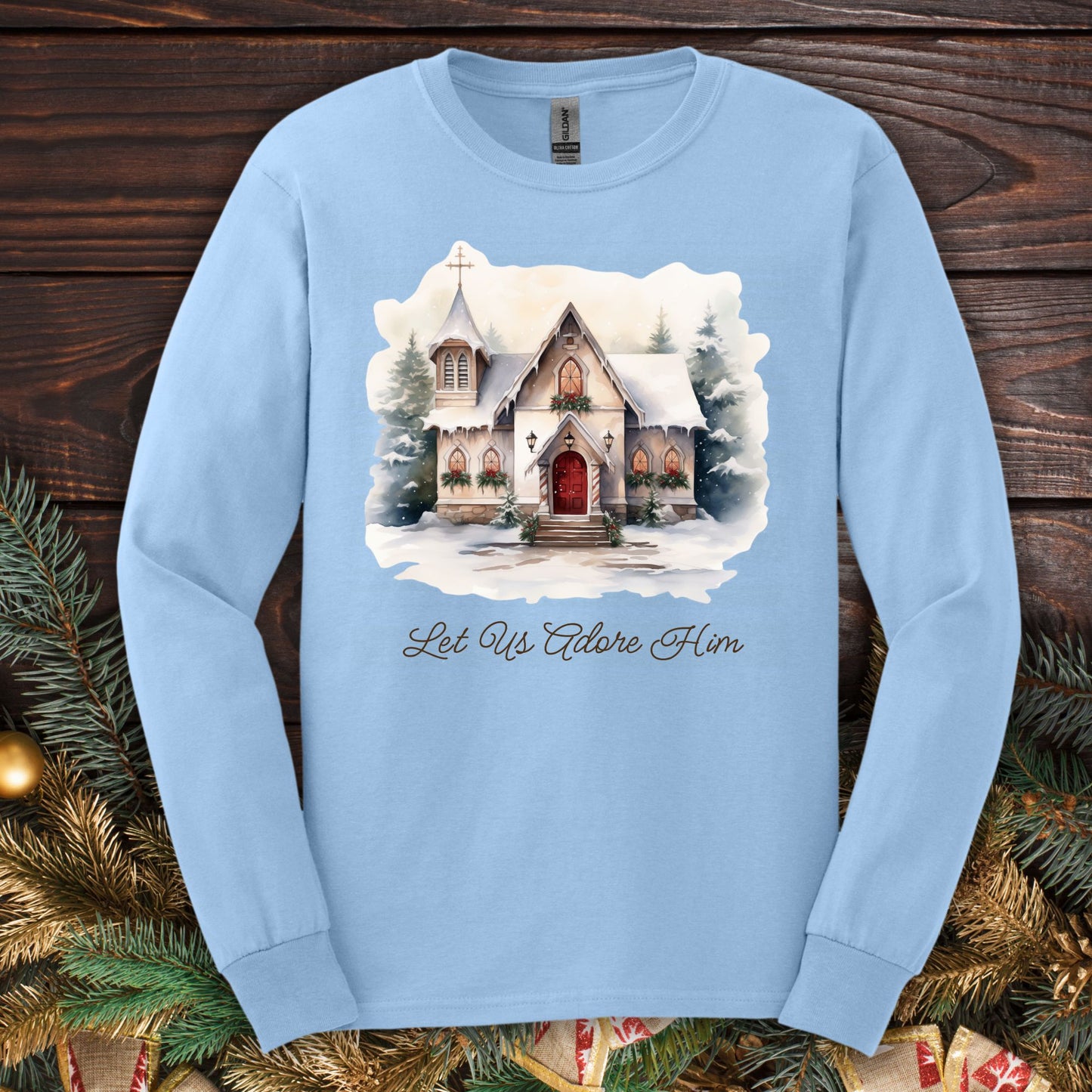 Light blue long sleeve tee with a watercolor snow-covered country chapel and "Let Us Adore Him" text.