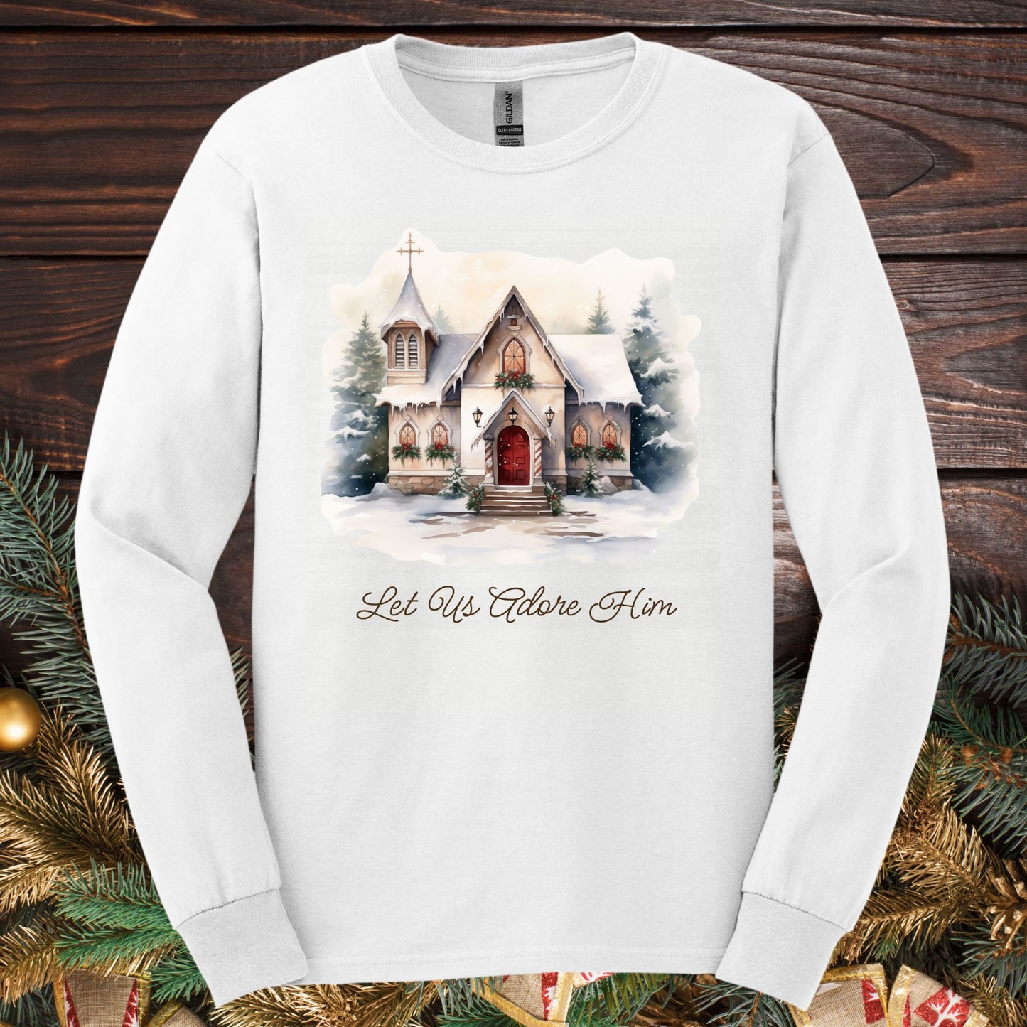 White long sleeve tee with a watercolor snow-covered country chapel and "Let Us Adore Him" text.