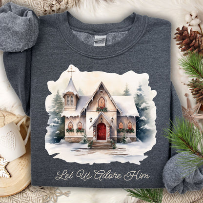 Dark heather Gildan sweatshirt with a snowy country chapel, evergreen garlands, wreaths, and "Let Us Adore Him" text.