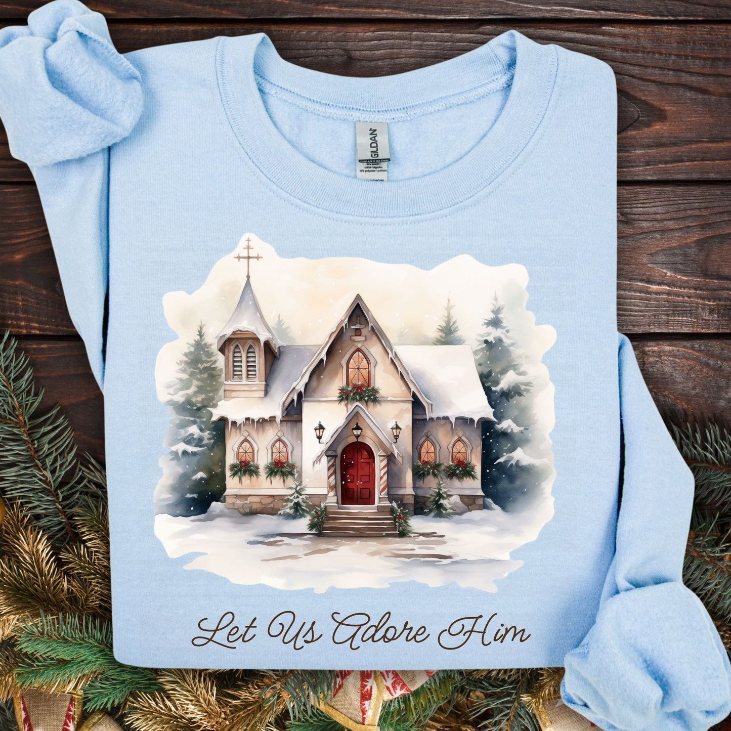 Light blue Gildan fleece sweatshirt with a snowy country chapel, garlands, wreaths, and "Let Us Adore Him" text.