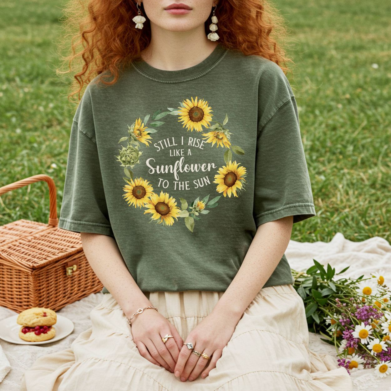 Garment-dyed olive green cotton t-shirt with a sunflower wreath and "Still I Rise" text.