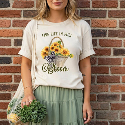 young woman wearing a t-shirt with a sunflower design and text that reads "Live Life in Full Bloom", standing against a brick wall.