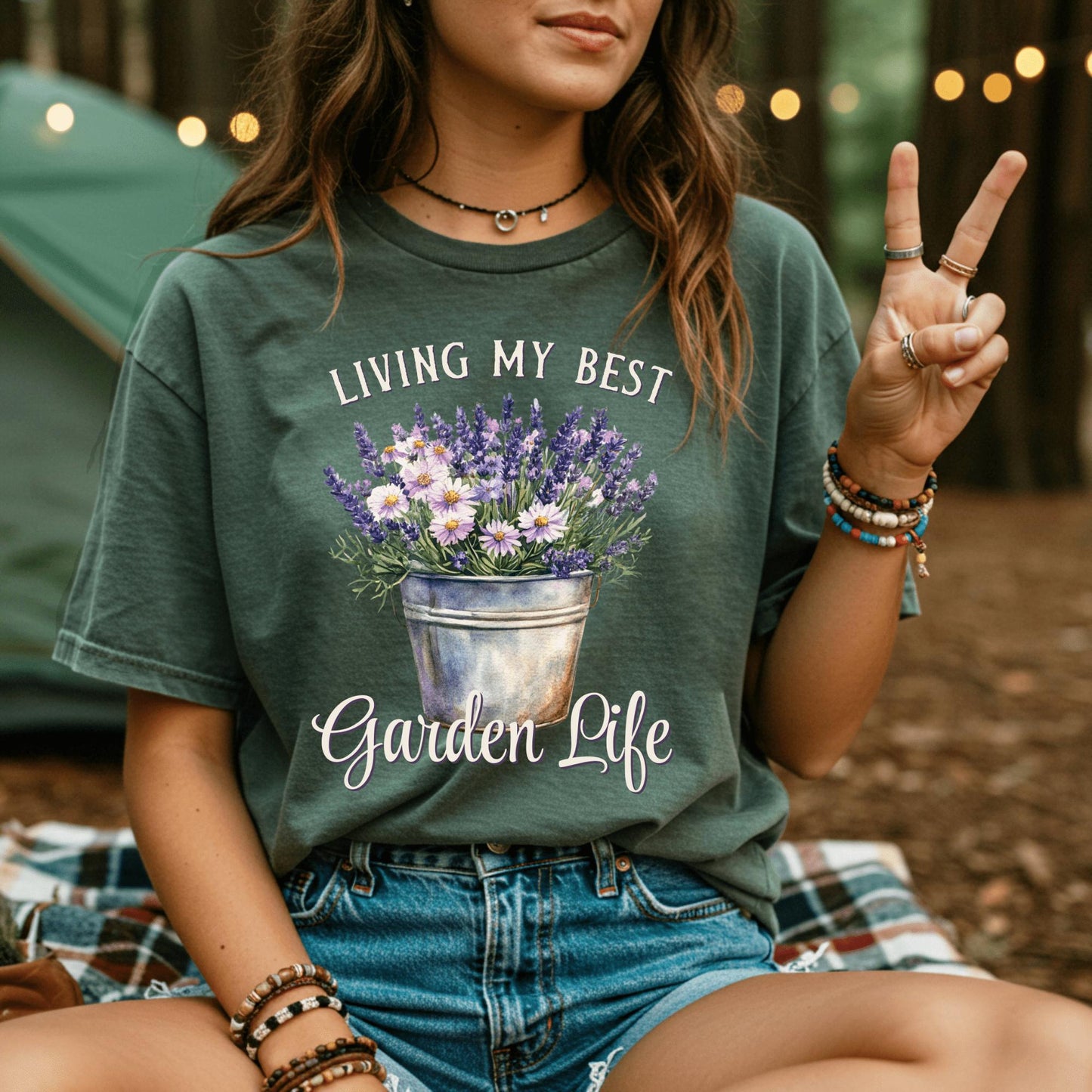 Woman wearing a dark green "Living My Best Garden Life" t-shirt with a lavender and daisy flower pot design.