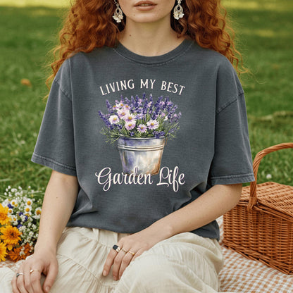 Woman in a charcoal gray "Living My Best Garden Life" t-shirt with a flower bucket graphic, sitting on a picnic blanket.