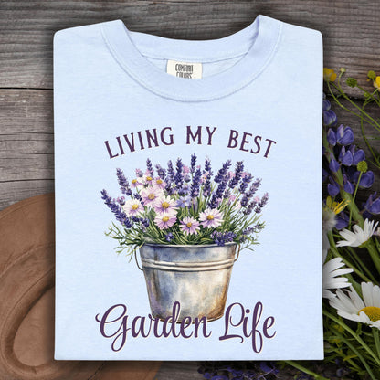 Folded hydrangea blue t-shirt with "Living My Best Garden Life" text and a lavender and daisy flower bucket graphic.