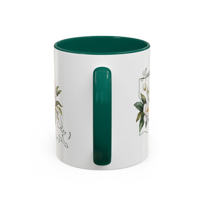 White ceramic mug with a glossy green interior and handle, featuring a delicate magnolia bouquet and Louisiana state outline.