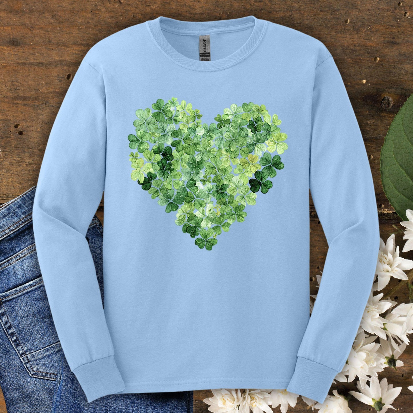 Light blue long sleeve tee with a heart made of green clover leaves, on a wooden background.