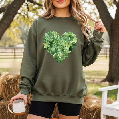 Woman wearing an olive green sweatshirt with a heart-shaped clover design, holding a mug outdoors.