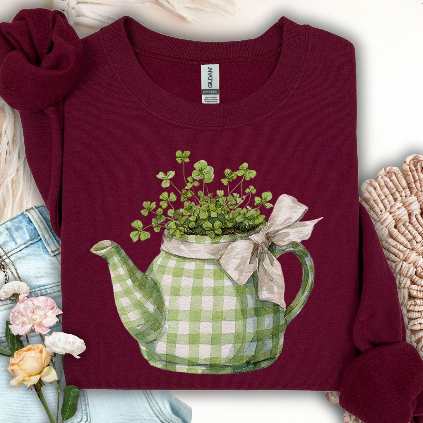 Maroon sweatshirt with a green checkered teapot design featuring a bow, surrounded by flowers and fabric.