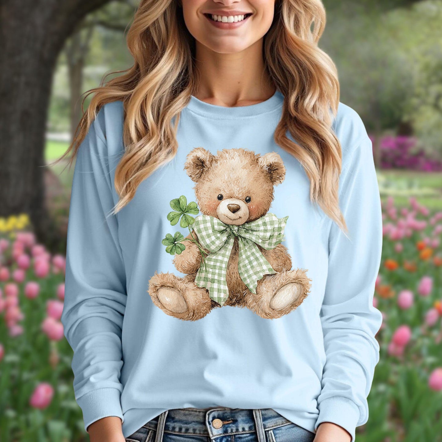 Watercolor teddy bear with checkered bow tie and four-leaf clovers on a light blue long-sleeve tee.