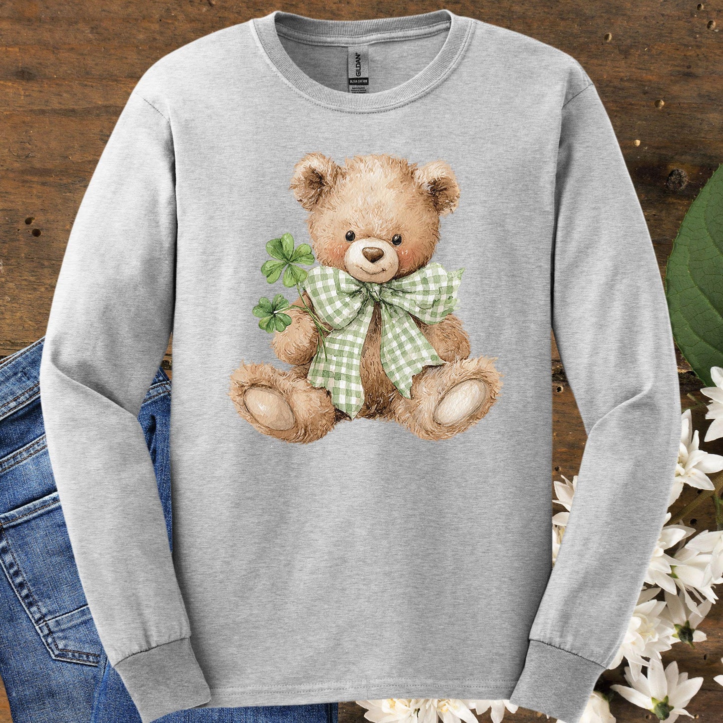 Ash long-sleeve tee with a watercolor teddy bear holding clovers and wearing a green checkered bow.