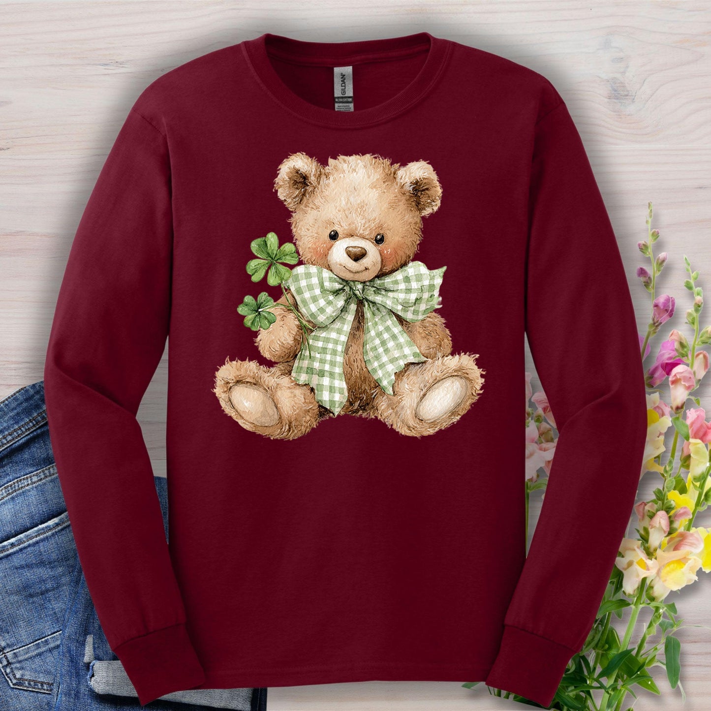 Maroon long-sleeve tee with a watercolor teddy bear wearing a checkered bow tie and holding clovers.