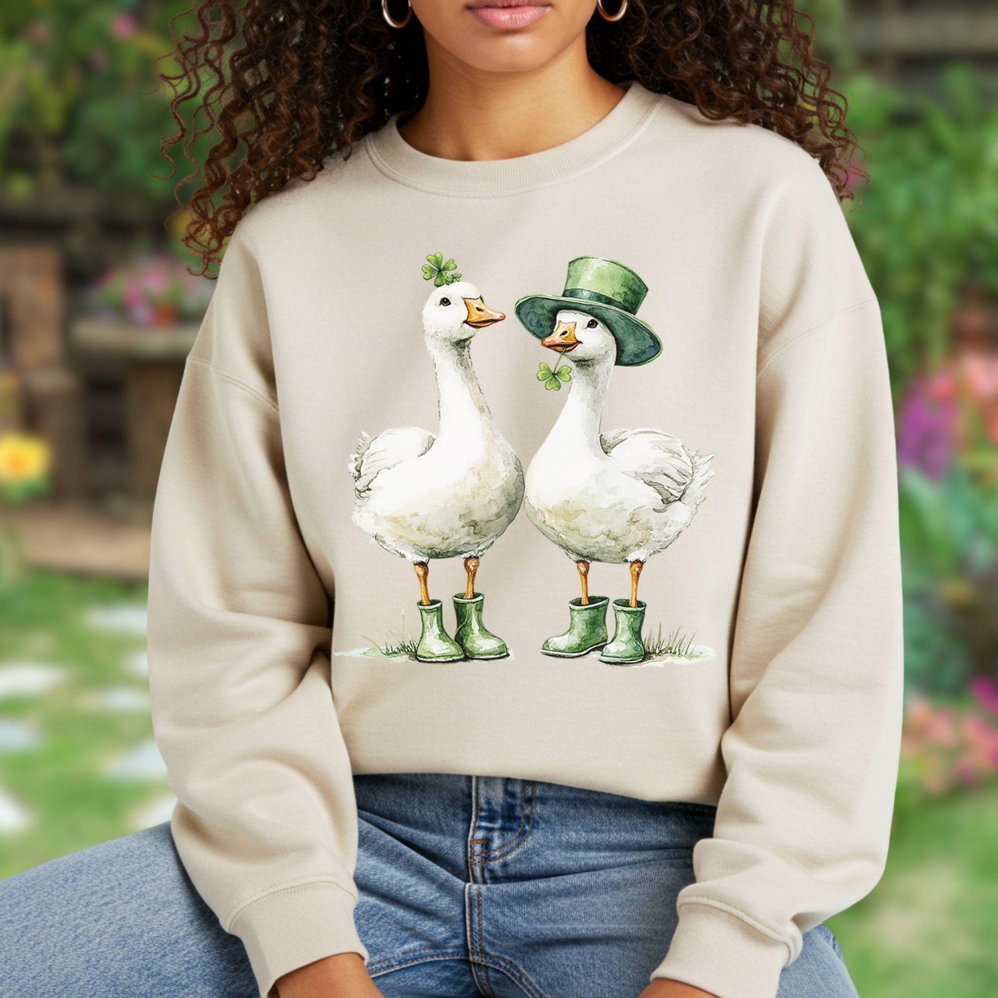 Beige sweatshirt with two white geese in green boots and St. Patrick's Day hats and shamrocks.