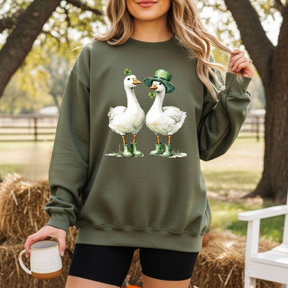 Olive green sweatshirt with two white geese in St. Patrick's Day attire, one with a shamrock, one with a leprechaun hat.