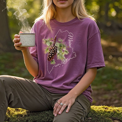 Garment-dyed plum t-shirt with a Maine outline and a hand-painted pine cone and branch design.