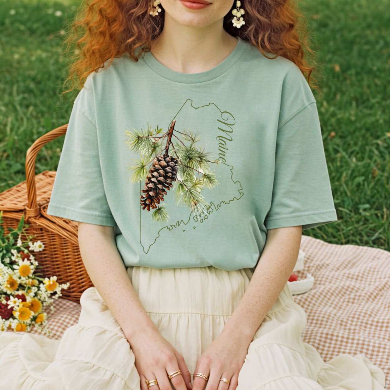 Relaxed-fit, garment-dyed sage green t-shirt with a pine cone and Maine outline graphic.