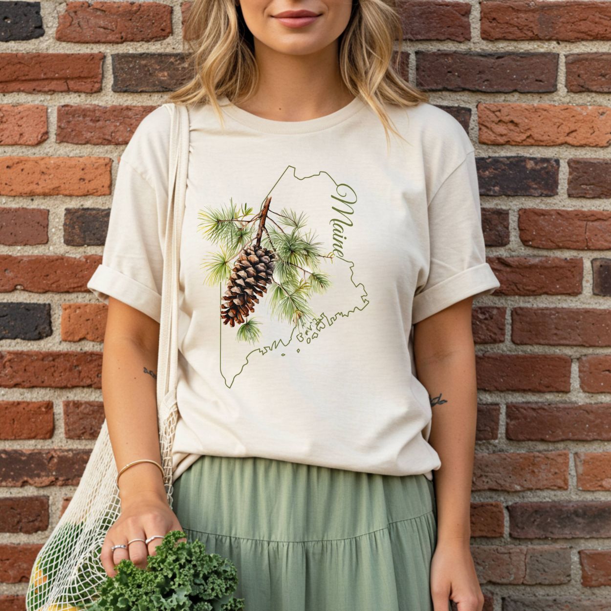 Relaxed-fit, garment-dyed cream t-shirt with a Maine outline, pine cone, and branch design.