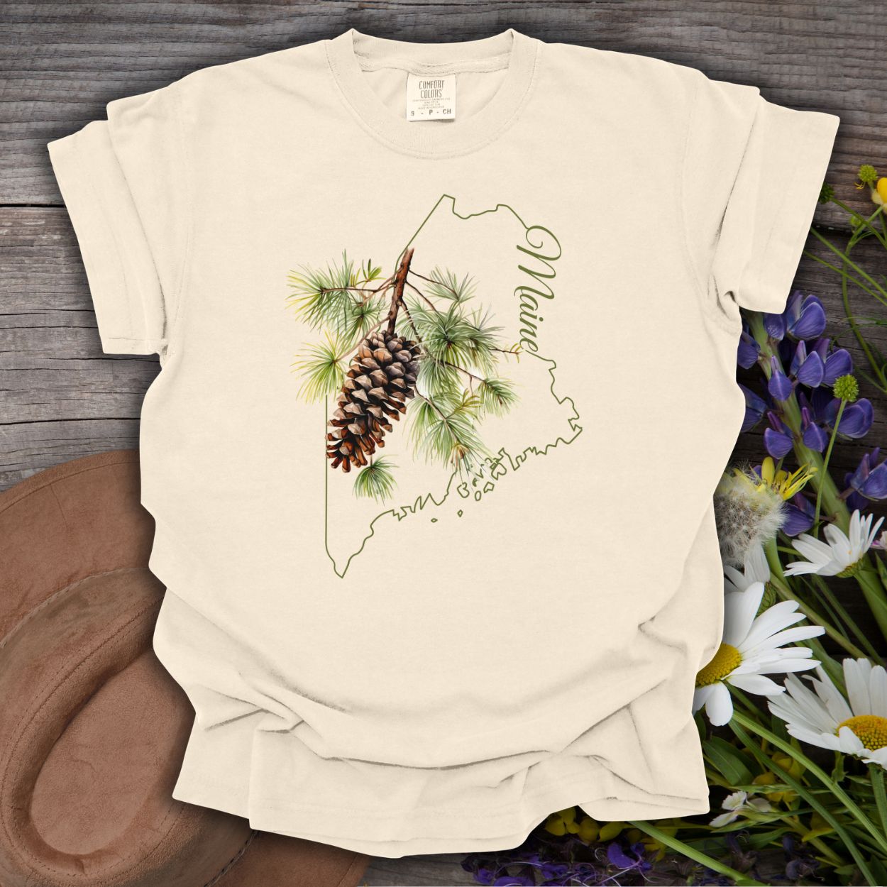 Ivory Maine State Flower T-shirt with a pine cone and branch design over a map of Maine.