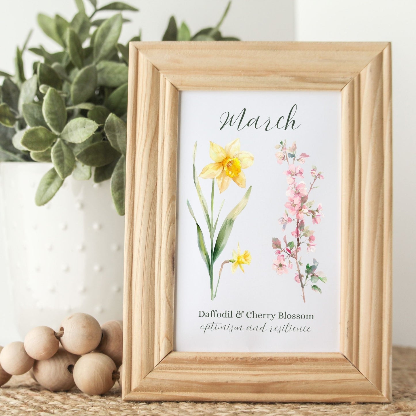 Watercolor daffodil and cherry blossom art print in a natural wood frame, featuring "March" and floral meanings.
