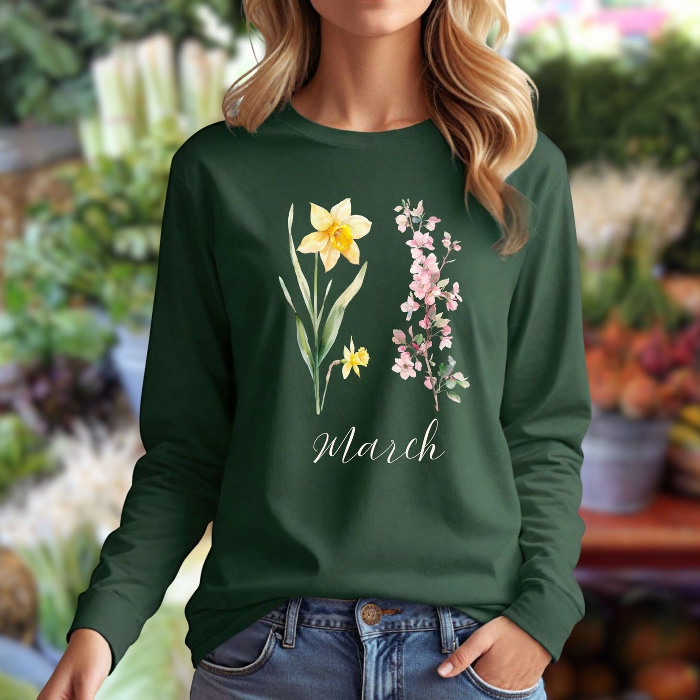 Woman wearing a dark green long-sleeve tee with hand-drawn daffodils, pink cherry blossoms, and "March" script.