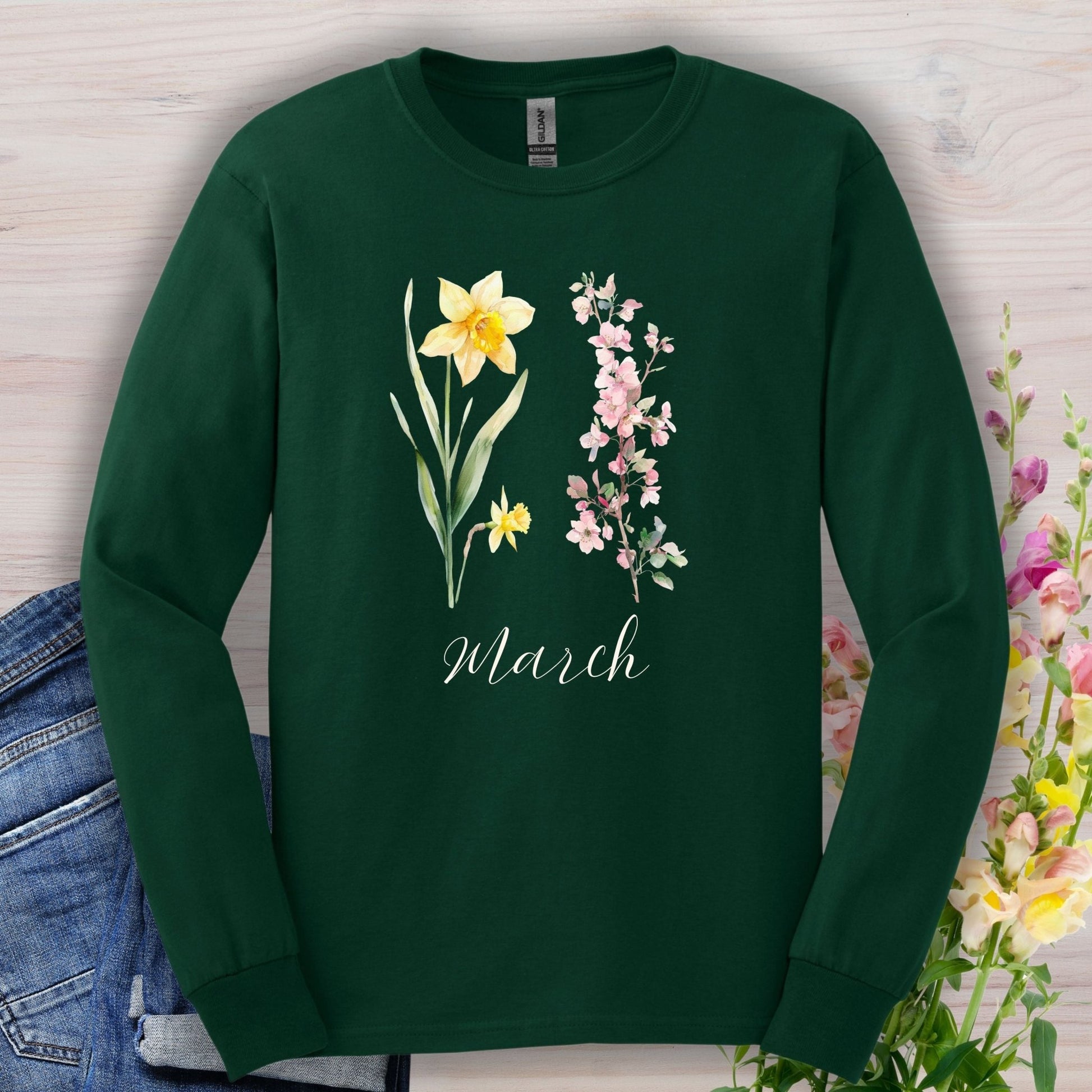 Forest Green long-sleeve tee with hand-drawn daffodil, pink cherry blossoms, and "March" script.