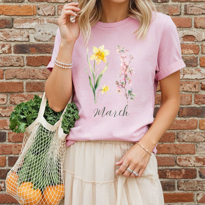 Pink garment-dyed cotton t-shirt with watercolor daffodils, cherry blossoms, and "March" script.