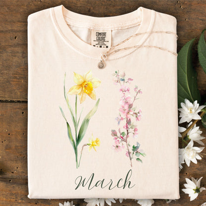 Ivory garment-dyed cotton t-shirt with watercolor daffodil, cherry blossoms, and "March" script.