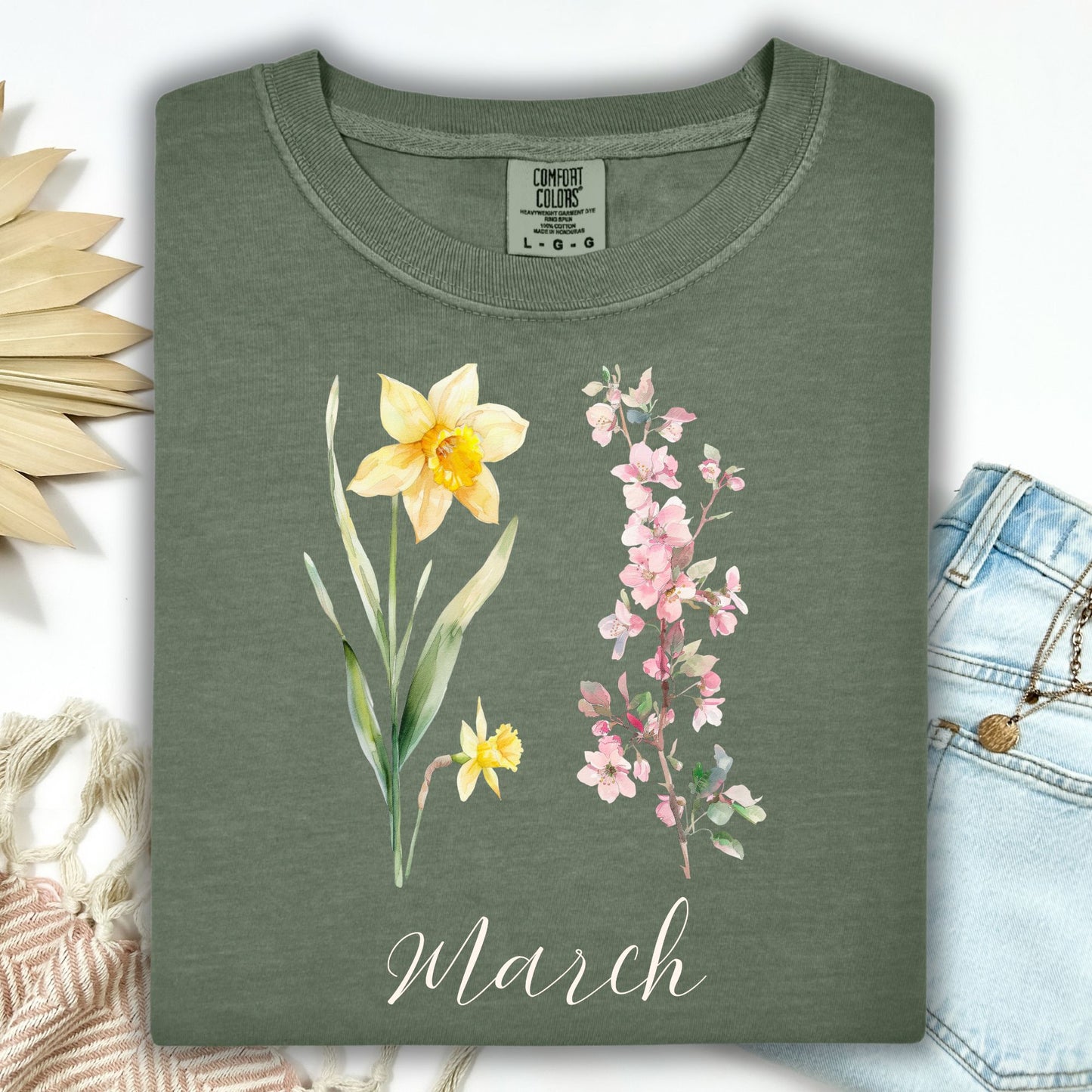 Moss green garment-dyed t-shirt with watercolor daffodils, cherry blossoms, and "March" script.
