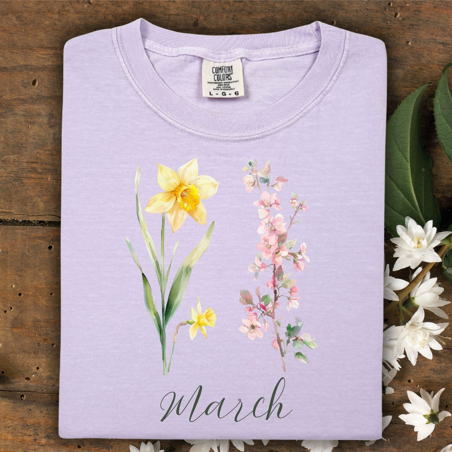 Orchid garment-dyed cotton t-shirt with watercolor daffodil, cherry blossoms, and "March" script.