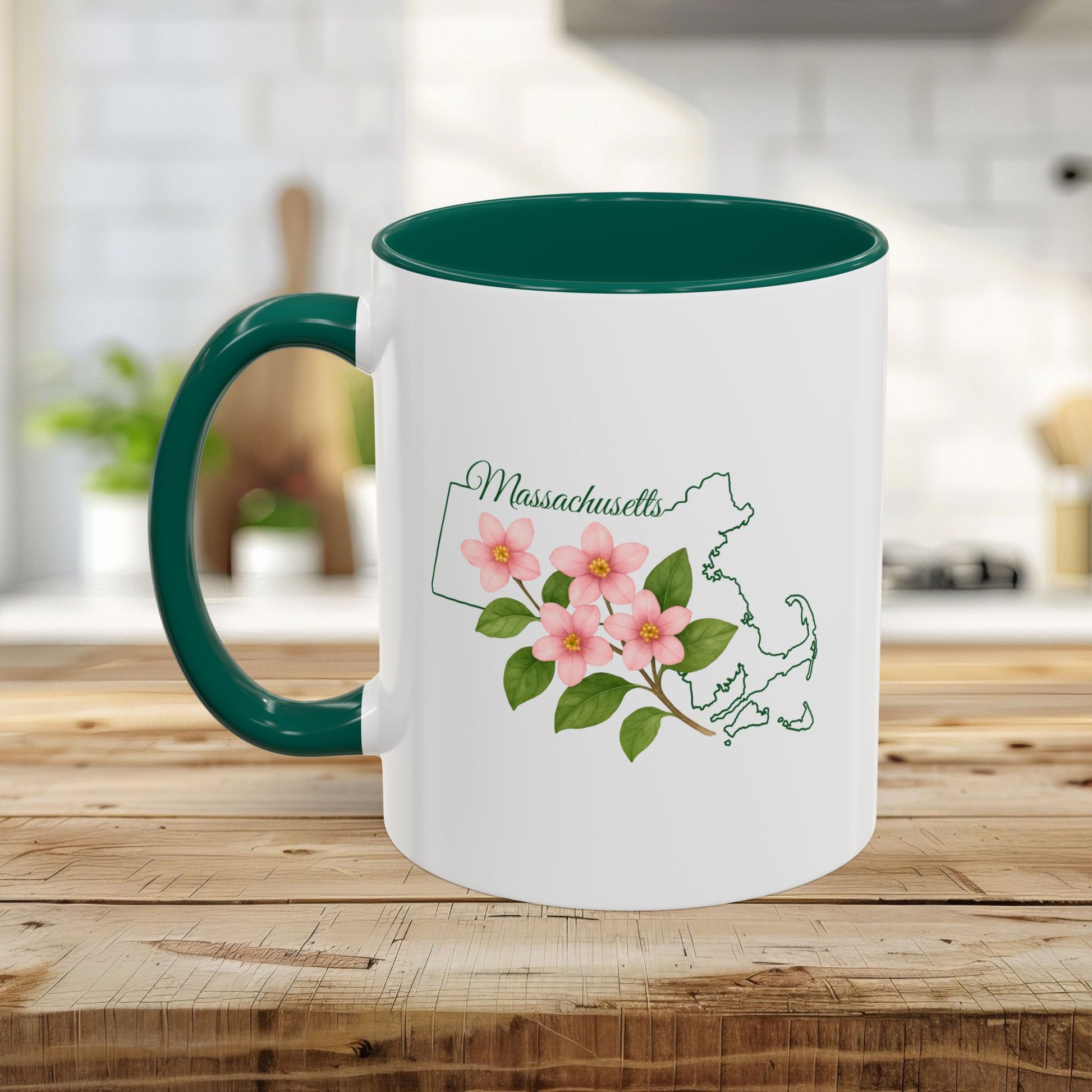 White ceramic mug with a dark green handle and interior, featuring a pink Mayflower design over a Massachusetts state outline.