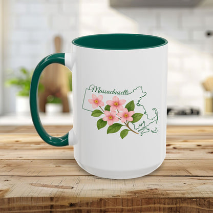 White ceramic mug with a green handle and interior, featuring a pink Mayflower design and Massachusetts state outline.
