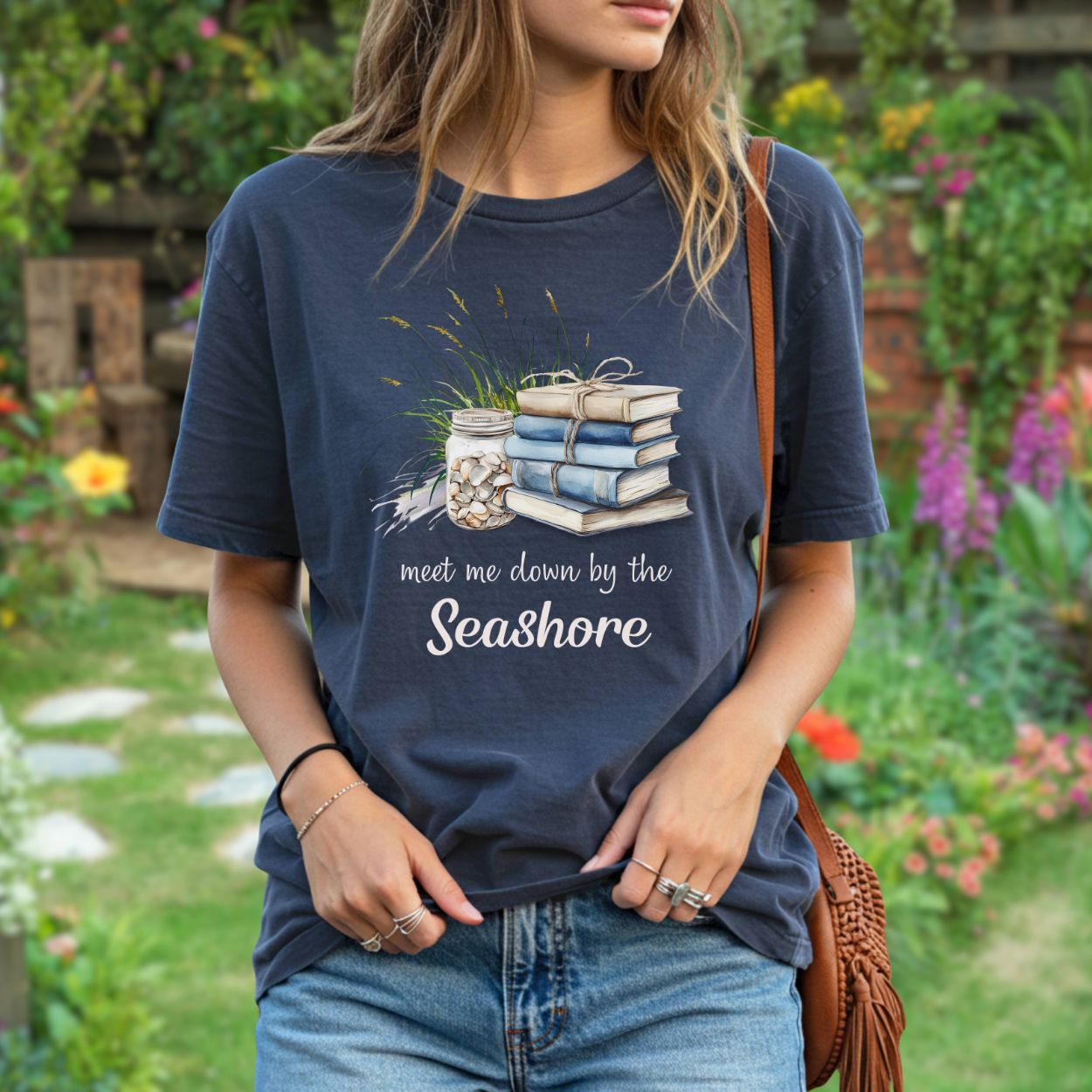 Garment-dyed navy t-shirt with a "Meet Me Down By the Seashore" graphic of stacked books, shells, and dune grass.