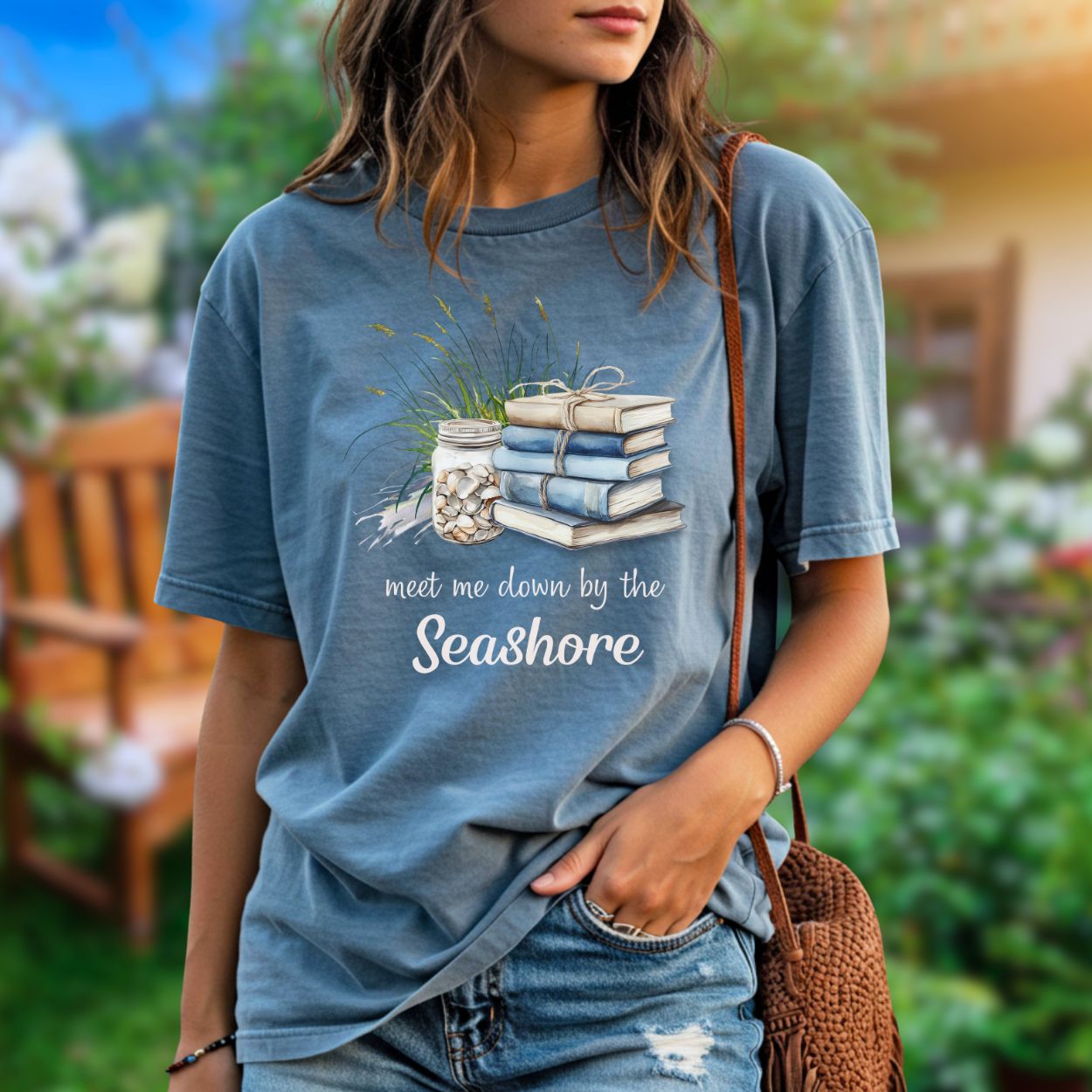 Garment-dyed blue t-shirt with "Meet Me Down By the Seashore" text and beach book graphic.